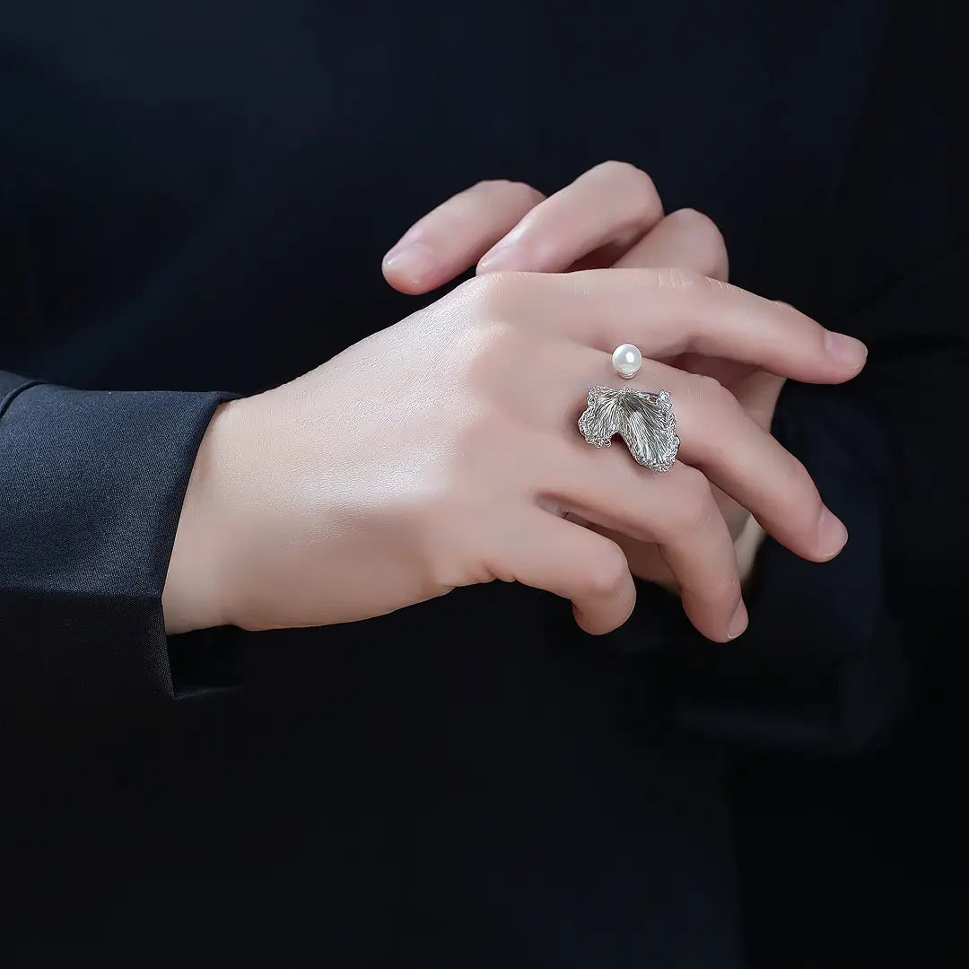 Aiko Tanaka Shiro Tsubasa ring, a silver wing ring with a pearl, worn on the hand against a dark background