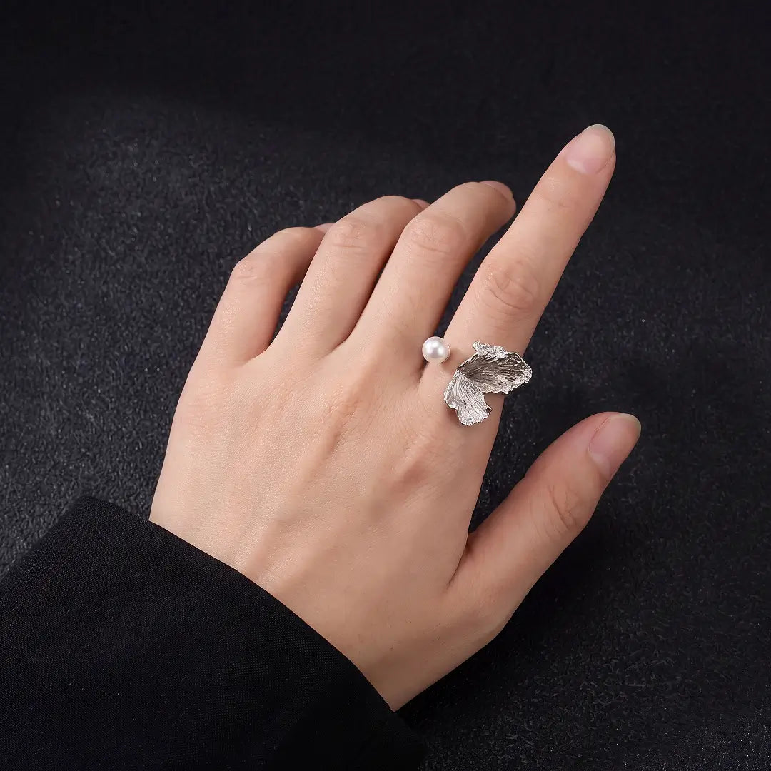 Aiko Tanaka Shiro Tsubasa ring, a silver wing and pearl open ring, worn on a finger against black fabric