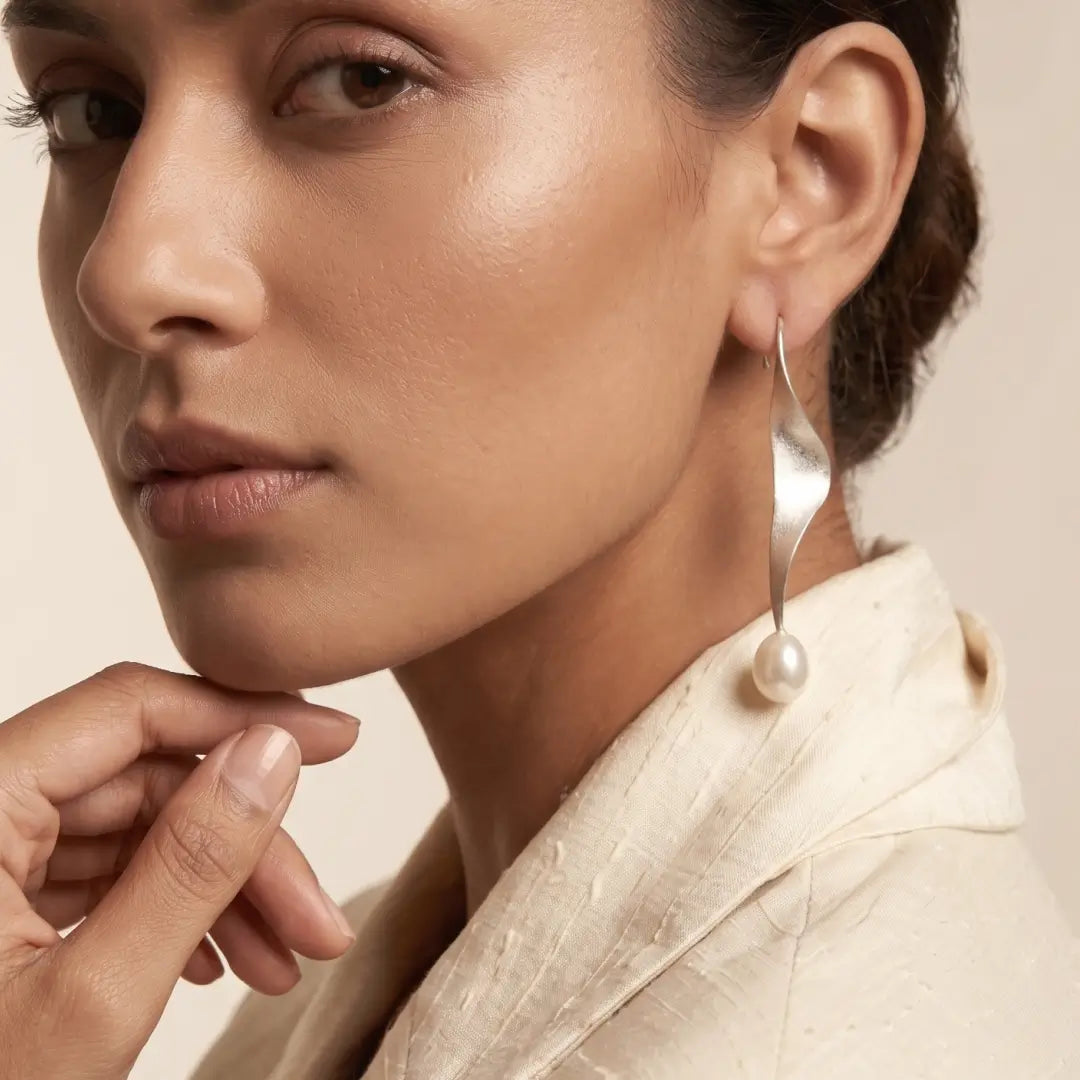 Aiko Tanaka Shizuku earrings, a long twisted silver drop with a white pearl, worn by a model in a cream top