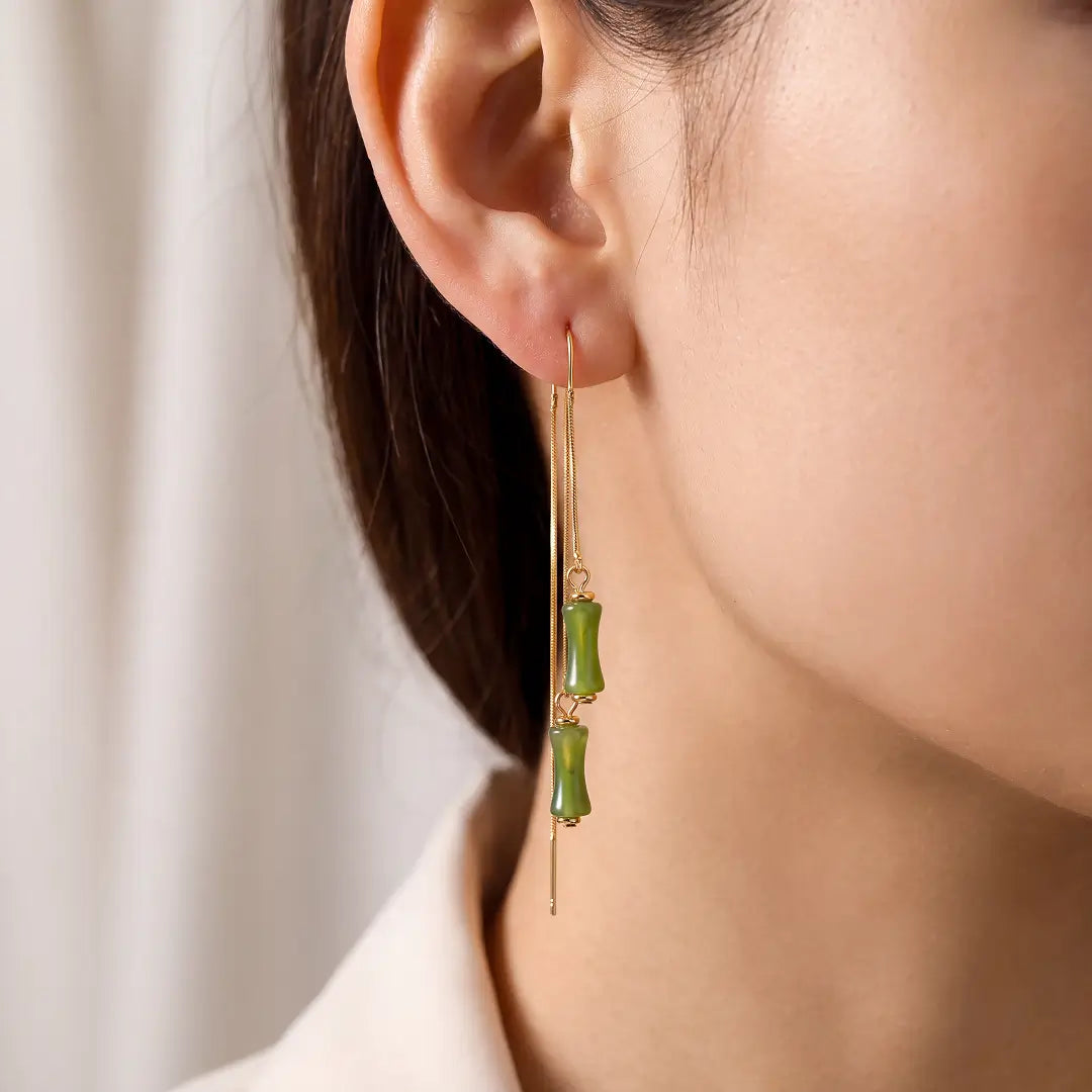 Aiko Tanaka Take no Kaze earrings, a long gold threader with green bamboo drops, worn on the ear with a white top