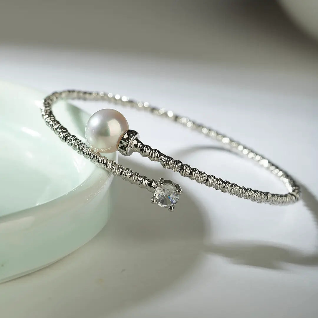 Aiko Tanaka Tsunagu bracelet, a crystal-lined silver cuff with a white pearl, resting beside a pale ceramic dish