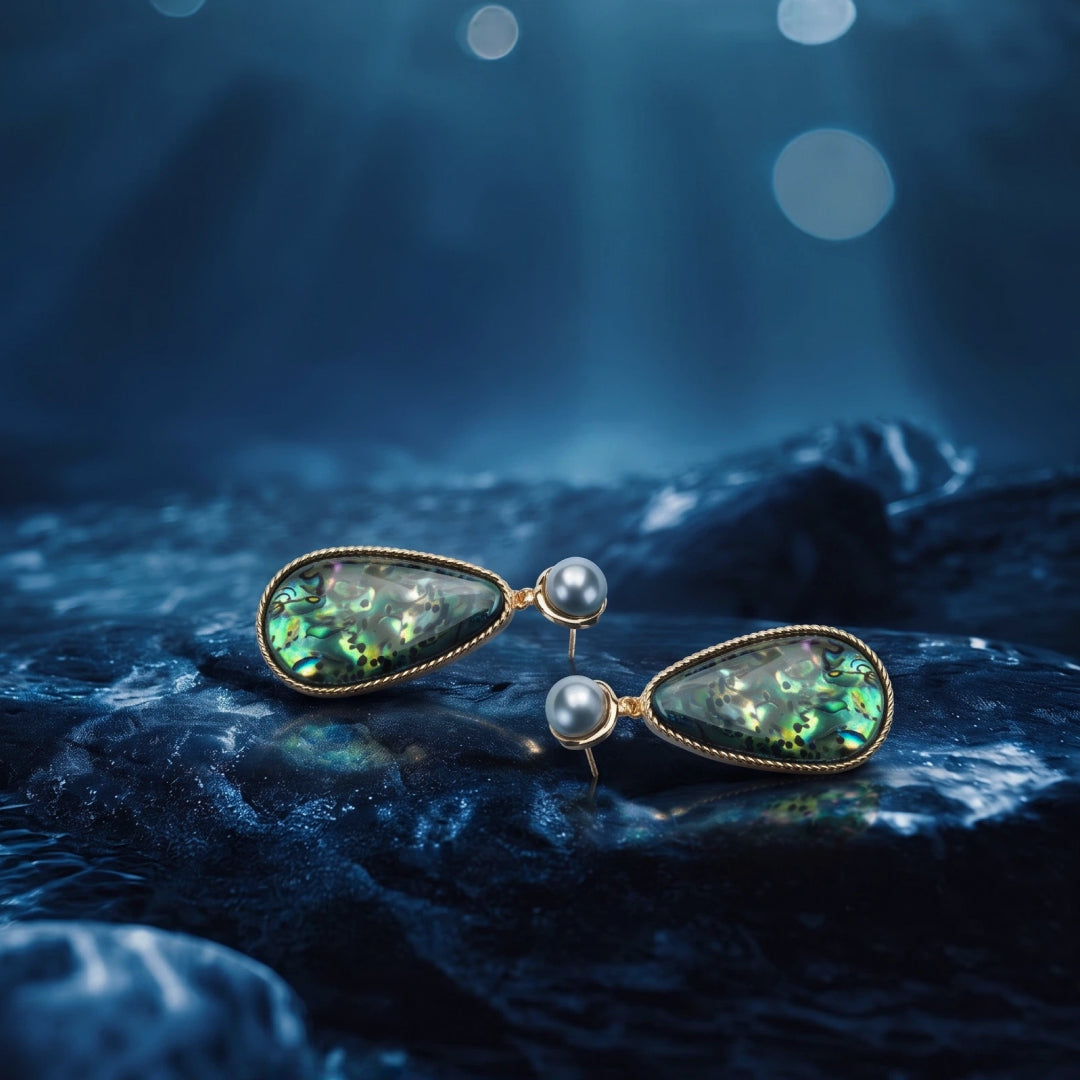 Aiko Tanaka Umi no Kagami abalone teardrop earrings with pearls resting on dark ocean rocks under blue water light