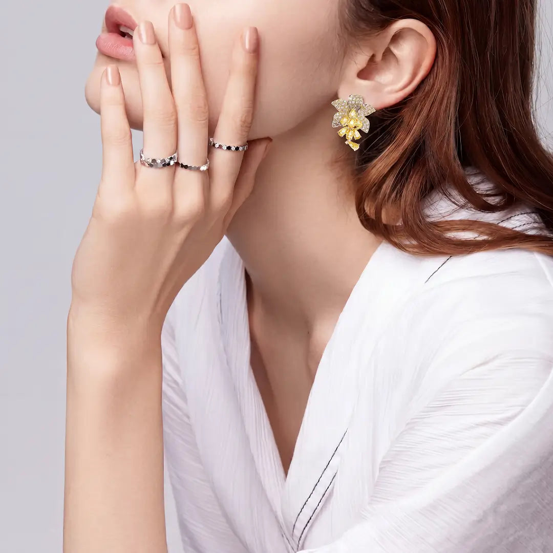 Woman in a white shirt touching her face, wearing Aiko Tanaka Yoka gold flower earrings and stacked rings