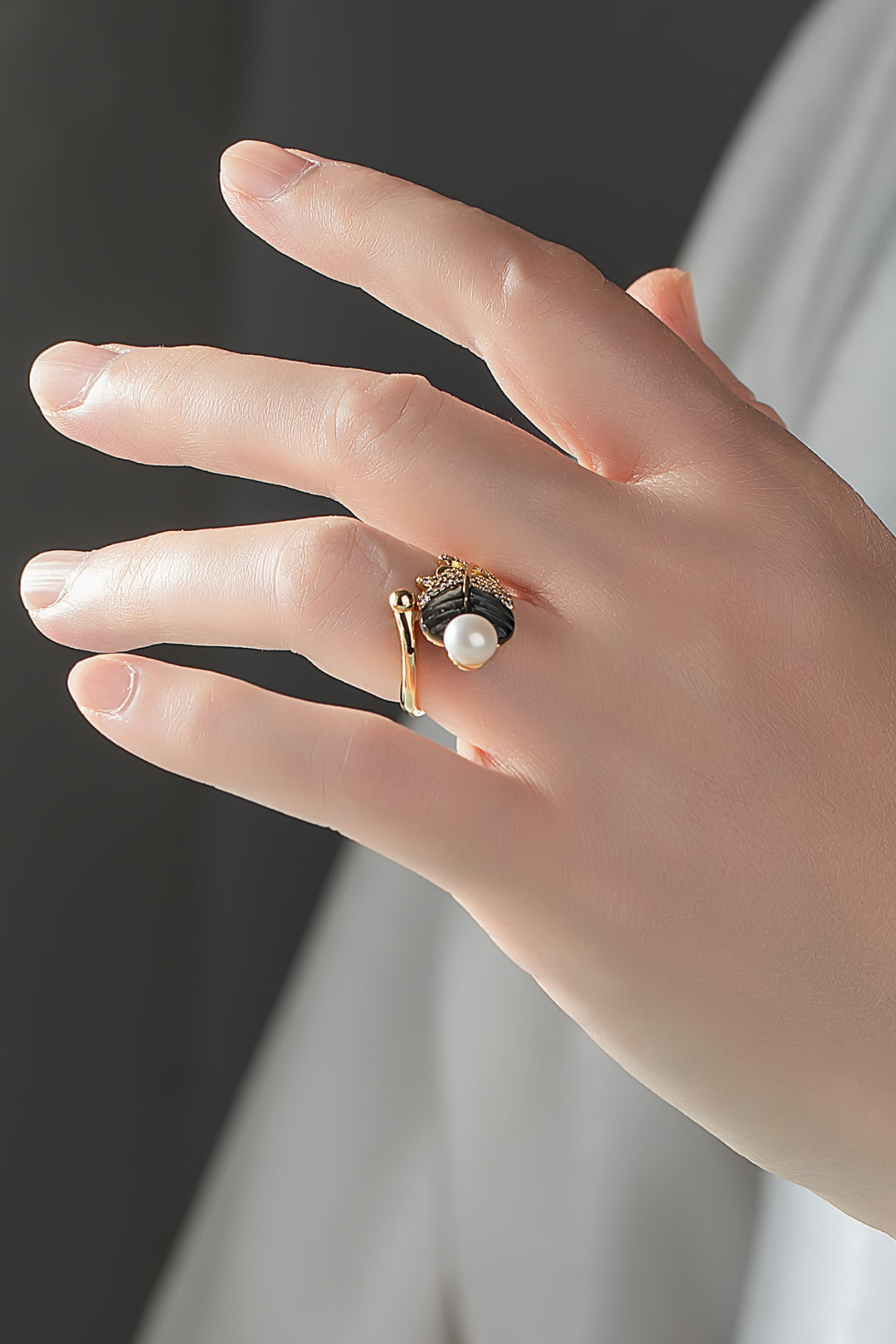 Close-up of a hand wearing the Aiko Tanaka Yoru no Ha gold ring with a smoky leaf and white pearl, dark backdrop
